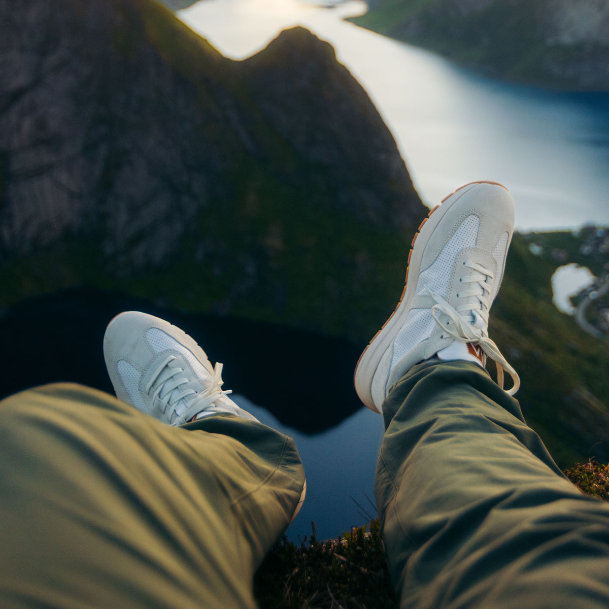 A man wearing the Hudson Leather Sneakers in White/Luggage while sitting on the edge of a cliff overlooking a body of water.