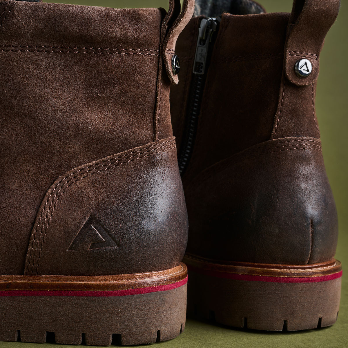 The Ryder boot in dark brown suede in front of a green backdrop.