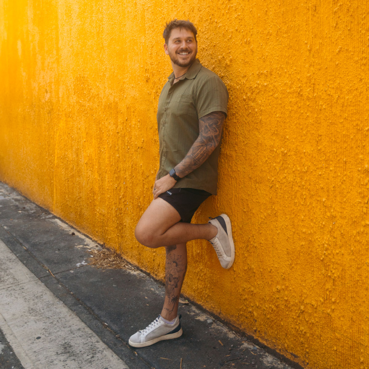 A man wearing the Donovan in off white is leaning against an orange wall. Shop Donovan