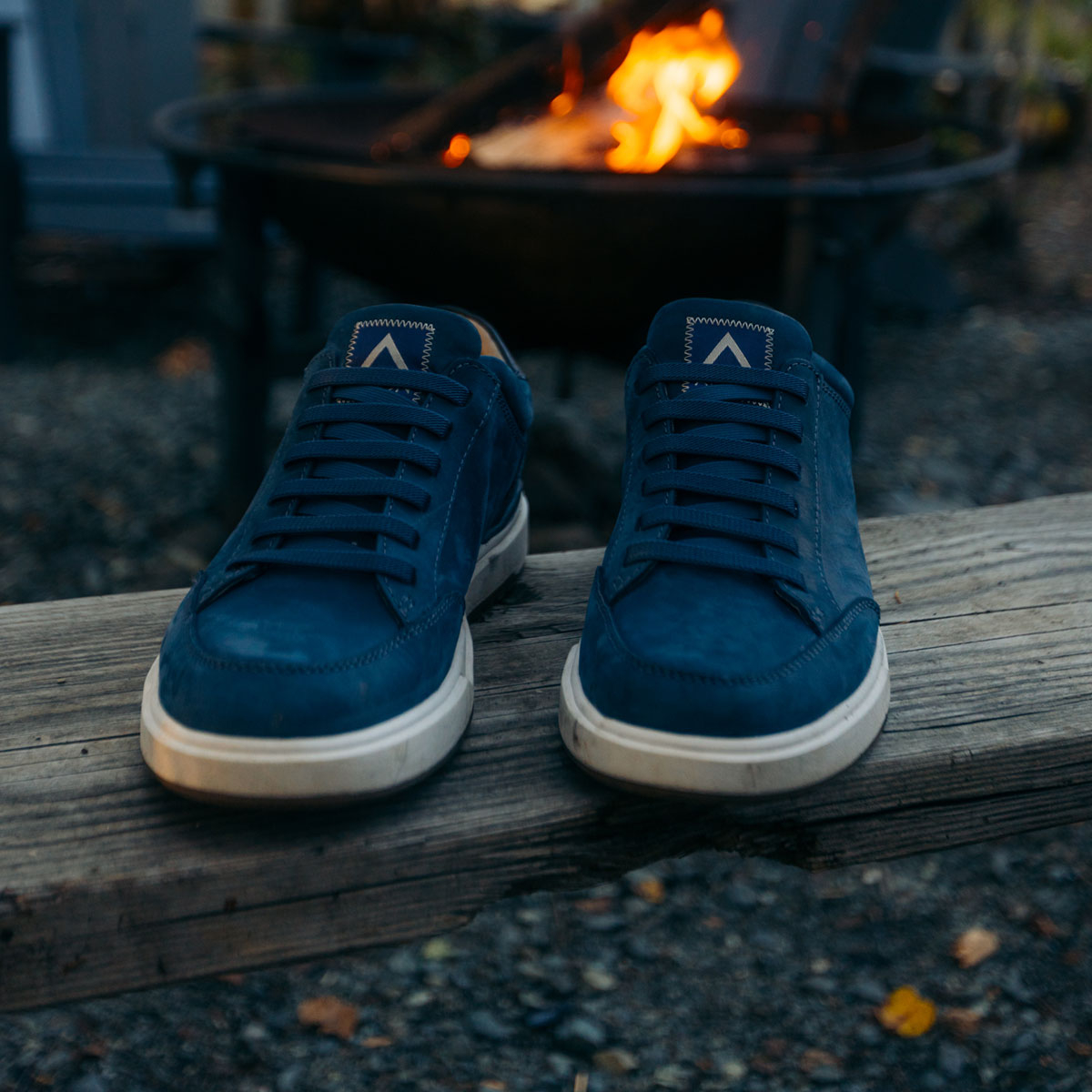 The Jenson Stretch-Lace Slip On Sneaker in True Blue on a bench in front of a fire pit.