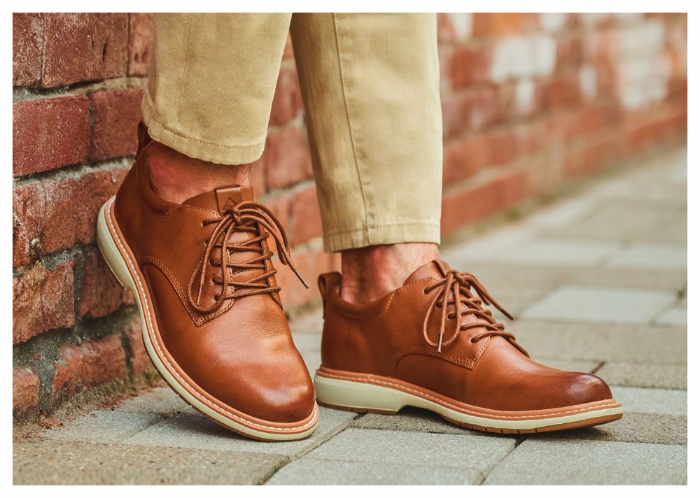 Man wearing the Atworth oxford dress shoe in brown leather against a brick wall.